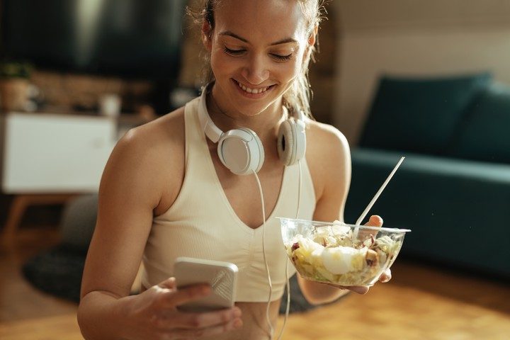 happy athletic woman texting on smart phone while eating salad a