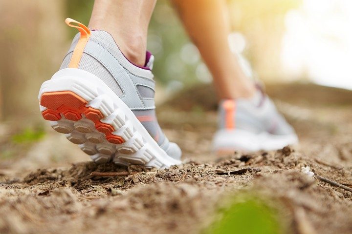 freeze action closeup of young woman walking or running on trail in forest or park in summer nature outdoors. athletic girl wearing sport shoes, exercising on footpath. selective focus on right sole